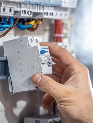 Mano de un electricista instalando un interruptor automático en un tablero eléctrico con cables visibles.